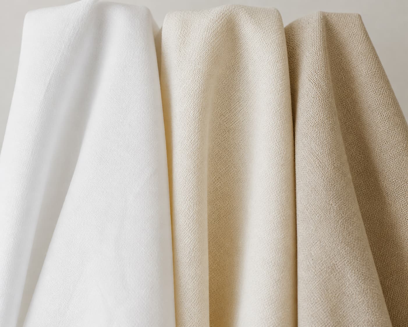 Trois échantillons de tissu blanc, crème et beige côte à côte sous une lumière naturelle douce.