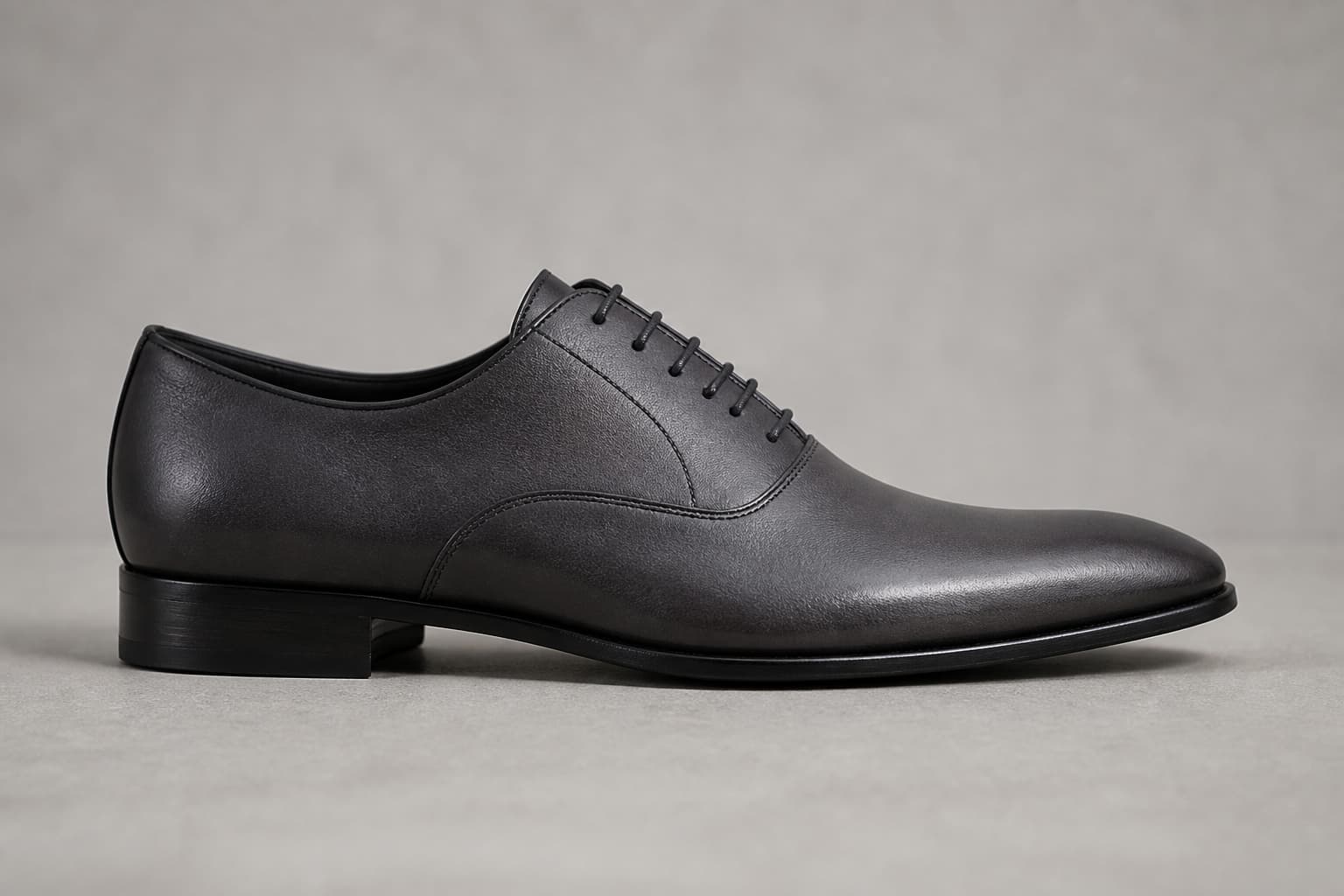 Richelieu gris anthracite en cuir lisse, vu de profil, avec un laçage fermé et une silhouette élancée, posé sur une surface sobre.