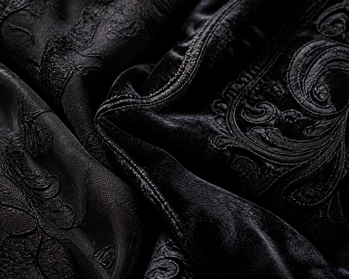 Gros plan sur un tissu noir texturé captant la lumière, révélant des reliefs brillants et un détail de couture.